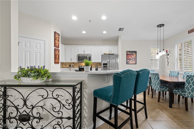 kitchen with kitchen peninsula, stainless steel appliances, decorative backsplash, hanging light fixtures, and white cabinets