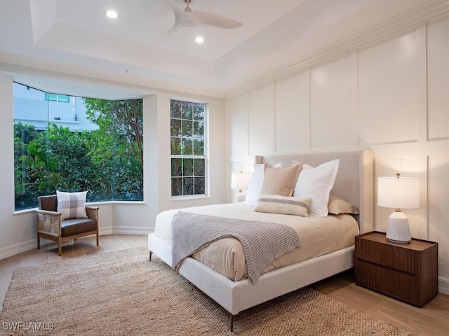 bedroom with a raised ceiling, ceiling fan, and light wood-type flooring