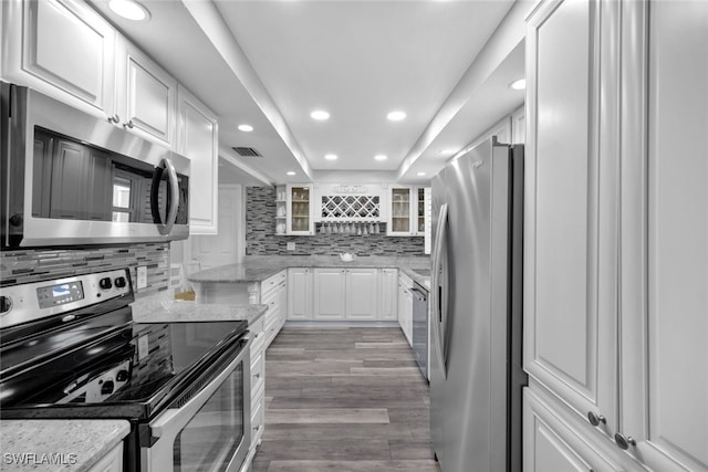 kitchen with tasteful backsplash, light hardwood / wood-style flooring, stainless steel appliances, light stone countertops, and white cabinets