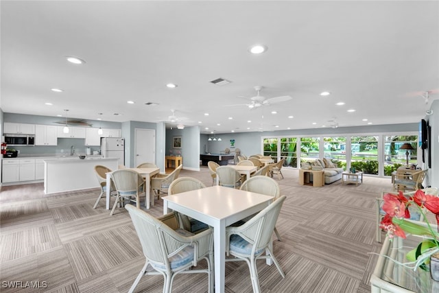 dining space featuring sink, light carpet, and ceiling fan