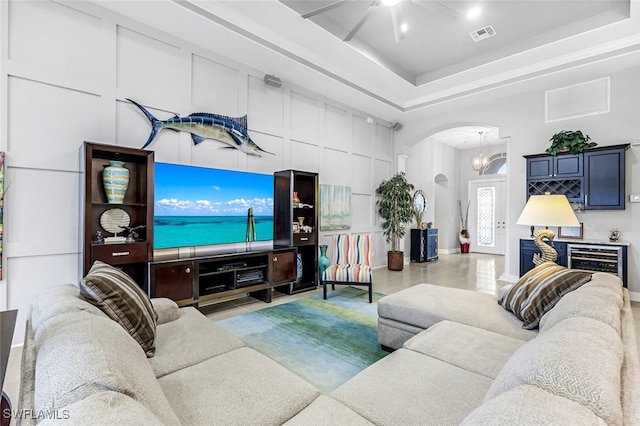 tiled living room featuring ceiling fan with notable chandelier, a tray ceiling, and wine cooler