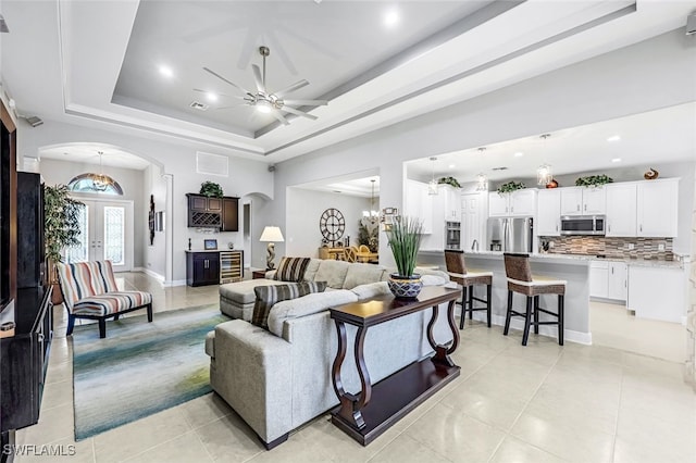 tiled living room featuring ceiling fan, a tray ceiling, and french doors