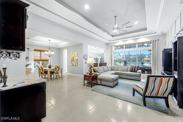 tiled living room with ceiling fan with notable chandelier and a raised ceiling