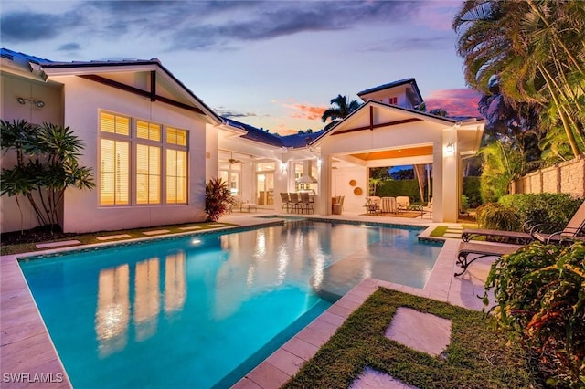 pool at dusk featuring ceiling fan and a patio