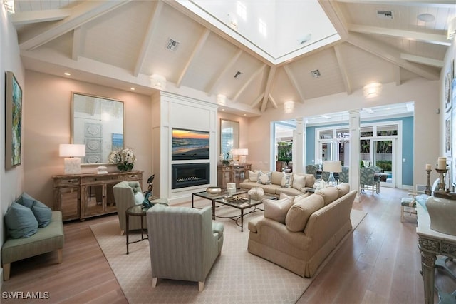 living room featuring light hardwood / wood-style flooring, beam ceiling, high vaulted ceiling, and ornate columns