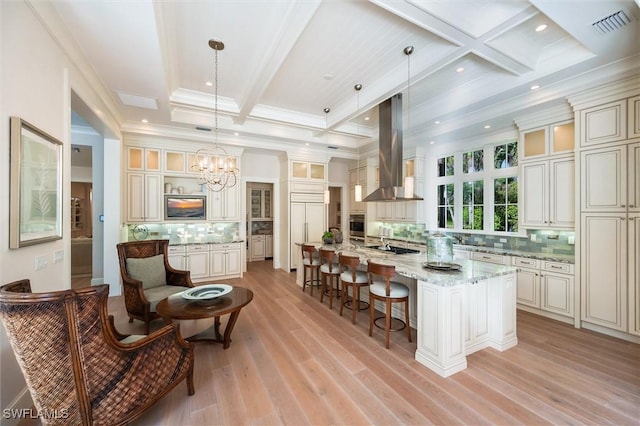 kitchen featuring light stone countertops, a large island with sink, decorative light fixtures, island exhaust hood, and decorative backsplash