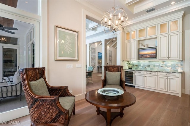 living area with crown molding, light hardwood / wood-style flooring, wine cooler, ceiling fan with notable chandelier, and coffered ceiling