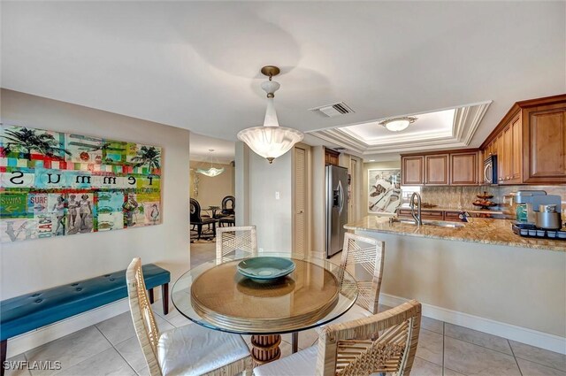 dining room featuring sink, light tile patterned floors, and a tray ceiling