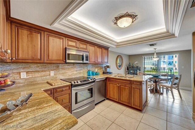 kitchen featuring light stone counters, kitchen peninsula, a raised ceiling, stainless steel appliances, and decorative backsplash