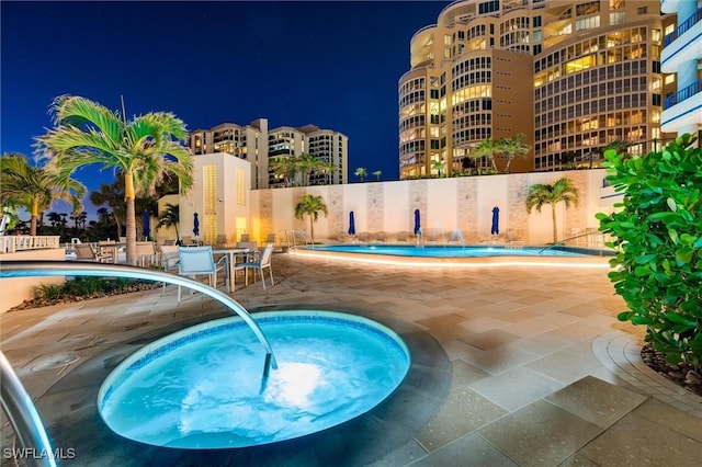 pool at twilight with a hot tub and a patio