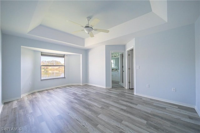 spare room with a raised ceiling, ceiling fan, and light hardwood / wood-style flooring