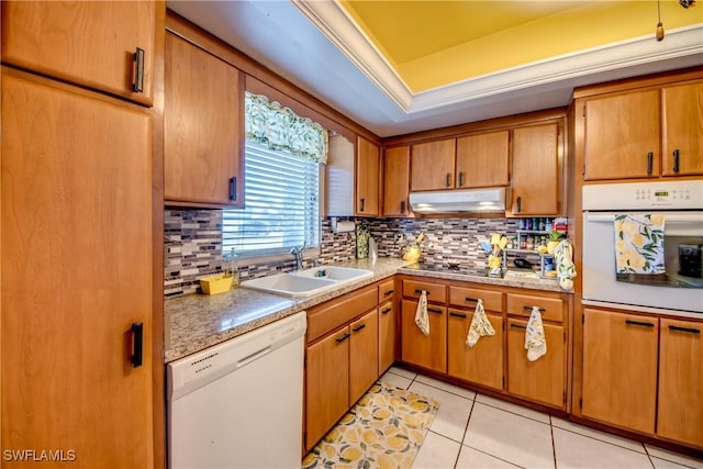 kitchen with sink, white appliances, light tile patterned floors, a tray ceiling, and decorative backsplash