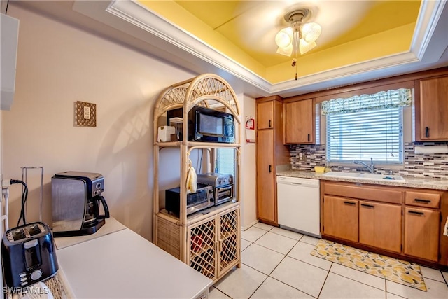 kitchen with light tile patterned flooring, dishwasher, sink, decorative backsplash, and a tray ceiling