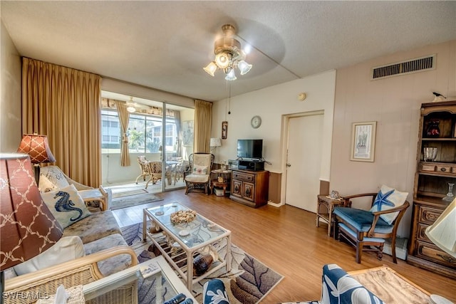 living room with ceiling fan, a textured ceiling, and light hardwood / wood-style flooring