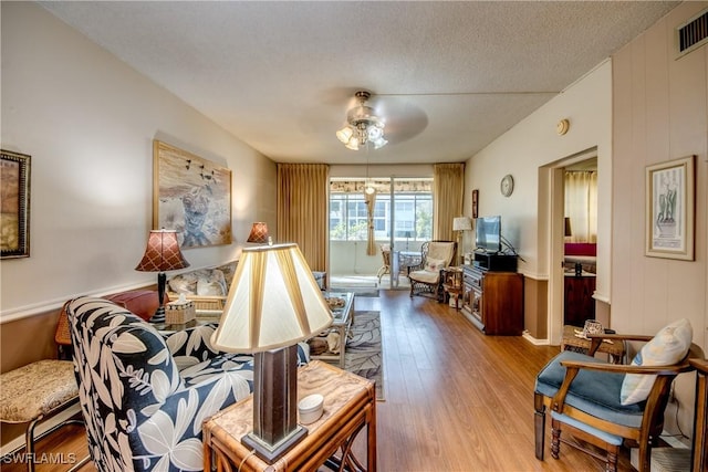 sitting room featuring ceiling fan, light hardwood / wood-style floors, a textured ceiling, and wood walls