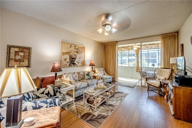 living room with hardwood / wood-style flooring, ceiling fan, and a textured ceiling