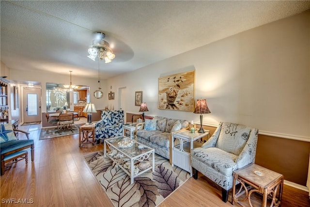 living room featuring wood-type flooring, ceiling fan with notable chandelier, and a textured ceiling