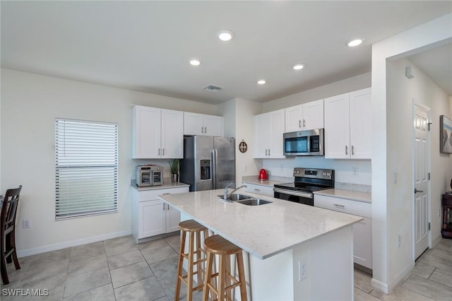 kitchen with white cabinetry, appliances with stainless steel finishes, a kitchen island with sink, light stone countertops, and sink