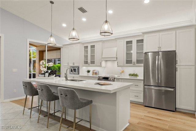 kitchen with a center island with sink, stainless steel appliances, custom range hood, vaulted ceiling, and white cabinets