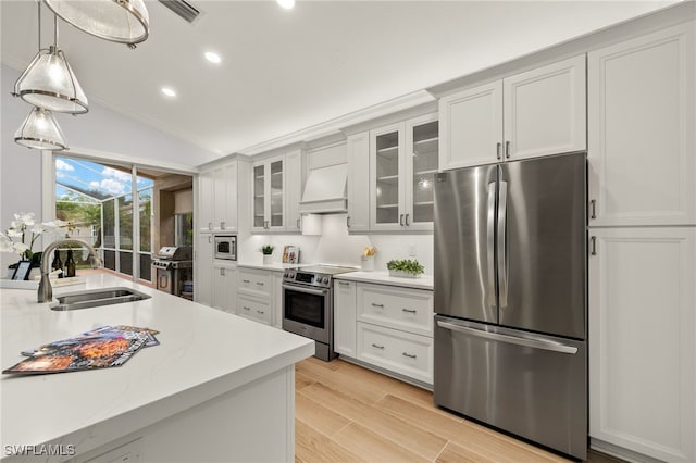 kitchen with appliances with stainless steel finishes, sink, premium range hood, and white cabinetry