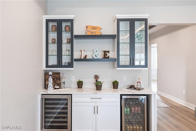 bar with light stone counters, light hardwood / wood-style floors, white cabinetry, and wine cooler