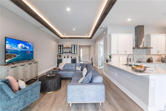 living room featuring a raised ceiling, sink, beverage cooler, and light hardwood / wood-style floors