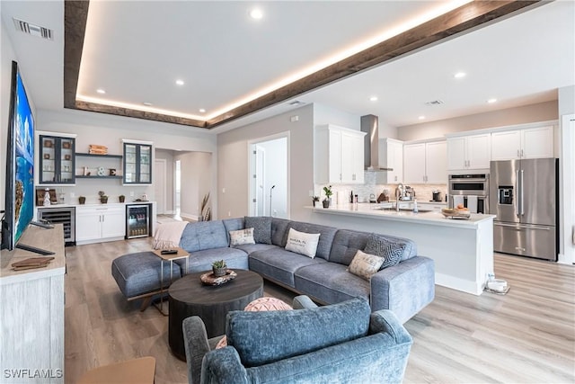 living room with sink, beverage cooler, and light hardwood / wood-style flooring