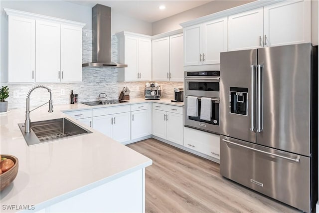 kitchen featuring appliances with stainless steel finishes, sink, white cabinets, and wall chimney range hood