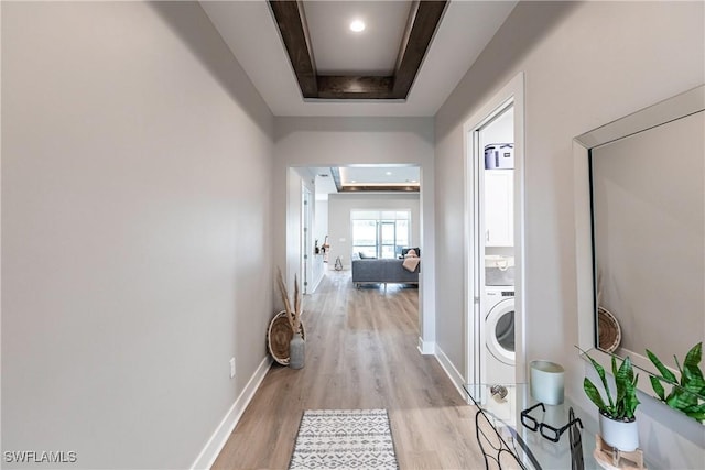 corridor featuring washer / dryer, a tray ceiling, and light hardwood / wood-style flooring