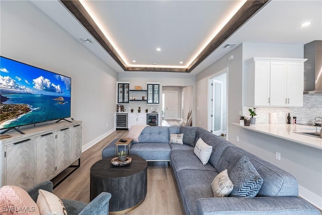 living room with hardwood / wood-style flooring, beverage cooler, and a tray ceiling