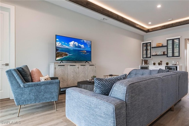 living room with a raised ceiling and light wood-type flooring