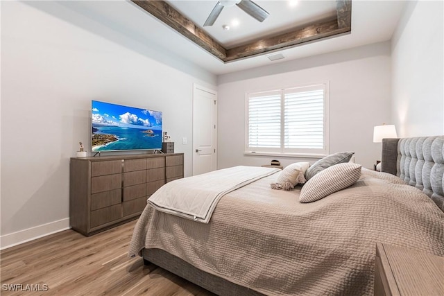 bedroom with ceiling fan, light hardwood / wood-style floors, and a raised ceiling