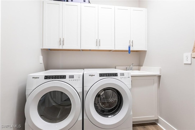 clothes washing area with cabinets, washer and clothes dryer, light hardwood / wood-style flooring, and sink