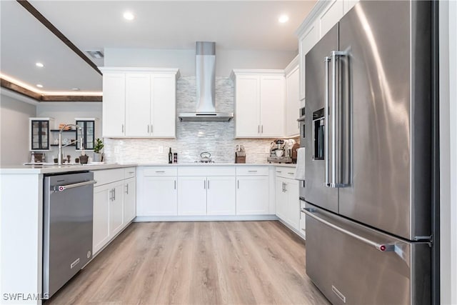 kitchen with tasteful backsplash, light hardwood / wood-style flooring, stainless steel appliances, white cabinets, and wall chimney exhaust hood