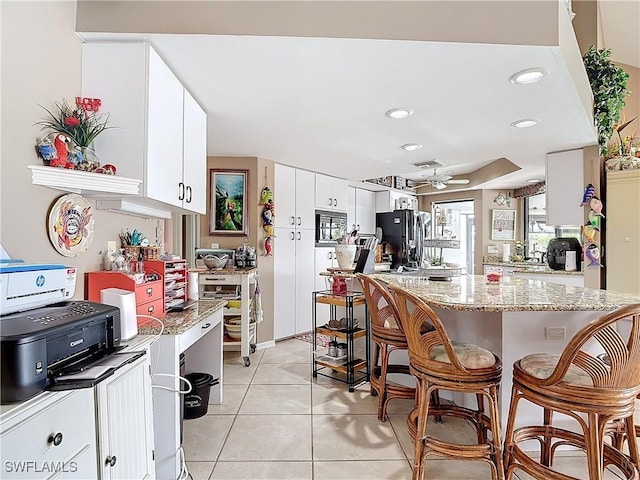 kitchen featuring white cabinetry, a kitchen breakfast bar, black fridge, ceiling fan, and light tile patterned floors