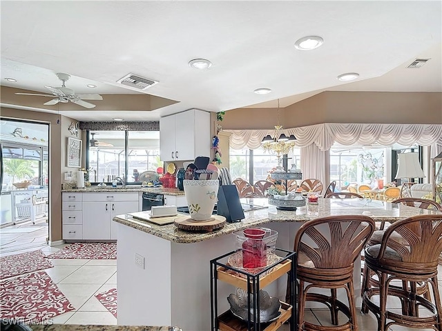 kitchen with white cabinets, ceiling fan with notable chandelier, light tile patterned floors, and a healthy amount of sunlight