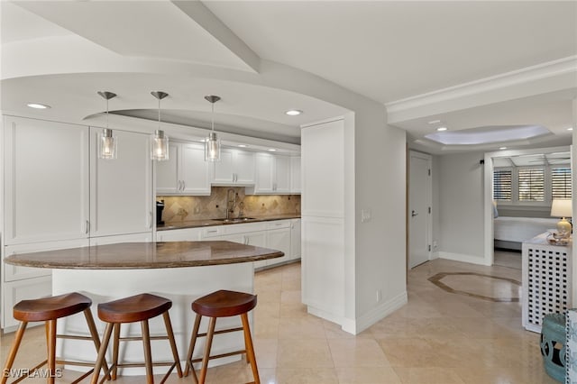 kitchen featuring a kitchen bar, white cabinetry, decorative backsplash, sink, and a raised ceiling