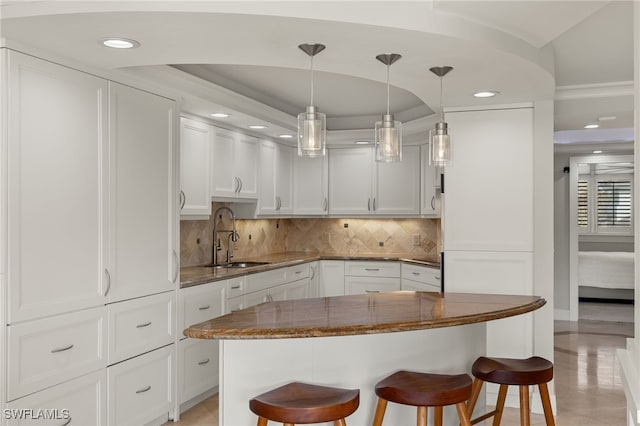 kitchen with pendant lighting, white cabinets, tasteful backsplash, dark stone countertops, and a breakfast bar