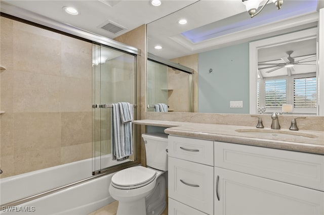 full bathroom with toilet, ceiling fan, a tray ceiling, vanity, and shower / bath combination with glass door