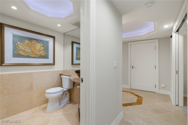 bathroom featuring toilet, tile walls, tile patterned floors, and a tray ceiling