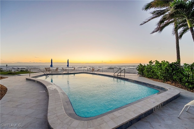 pool at dusk featuring a patio area and a water view