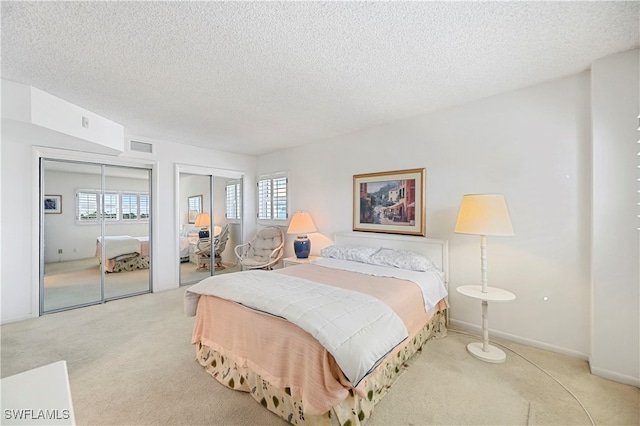 carpeted bedroom with a textured ceiling and multiple closets