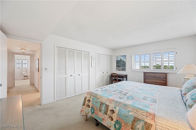 bedroom with a textured ceiling, two closets, and light colored carpet