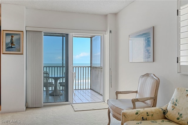 living area with light colored carpet, a textured ceiling, and a water view