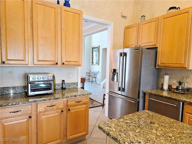 kitchen with stainless steel fridge, dark stone counters, and light tile patterned flooring