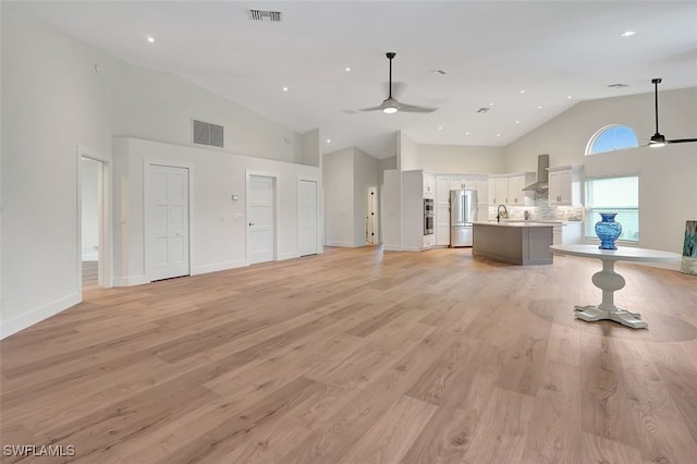 living room with ceiling fan, light wood-type flooring, sink, and a high ceiling