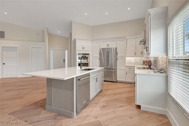 kitchen with a center island with sink, stainless steel appliances, vaulted ceiling, white cabinets, and sink