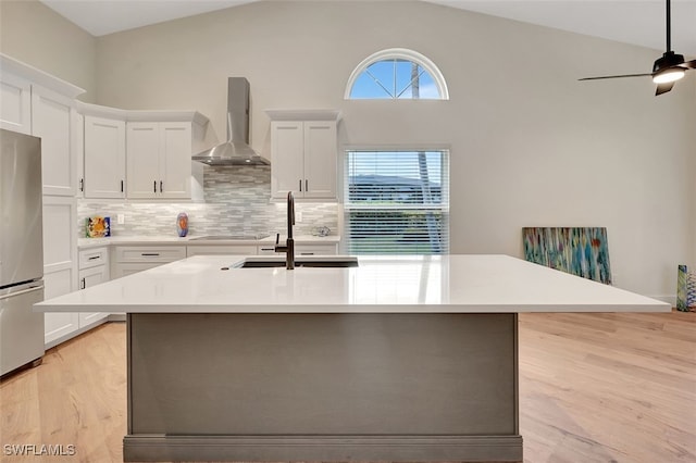 kitchen featuring tasteful backsplash, freestanding refrigerator, wall chimney exhaust hood, light countertops, and lofted ceiling