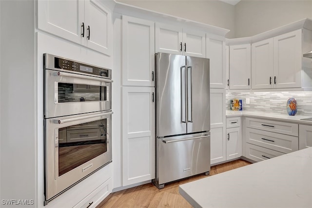 kitchen with backsplash, light countertops, light wood-style flooring, stainless steel appliances, and white cabinetry