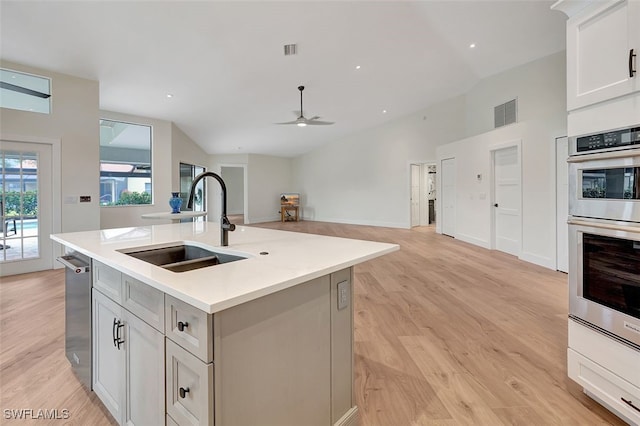 kitchen featuring ceiling fan, vaulted ceiling, sink, an island with sink, and stainless steel double oven